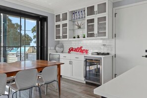 Une cuisine moderne avec des meubles blancs, une table à manger en bois et une porte vitrée donnant sur un balcon.