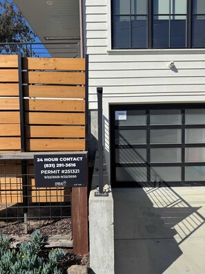 Een toegangspoort met houten omheining, een contactbord en een garage.