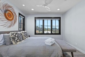 A modern bedroom with a large bed, a bench, and a view of the city through large windows.