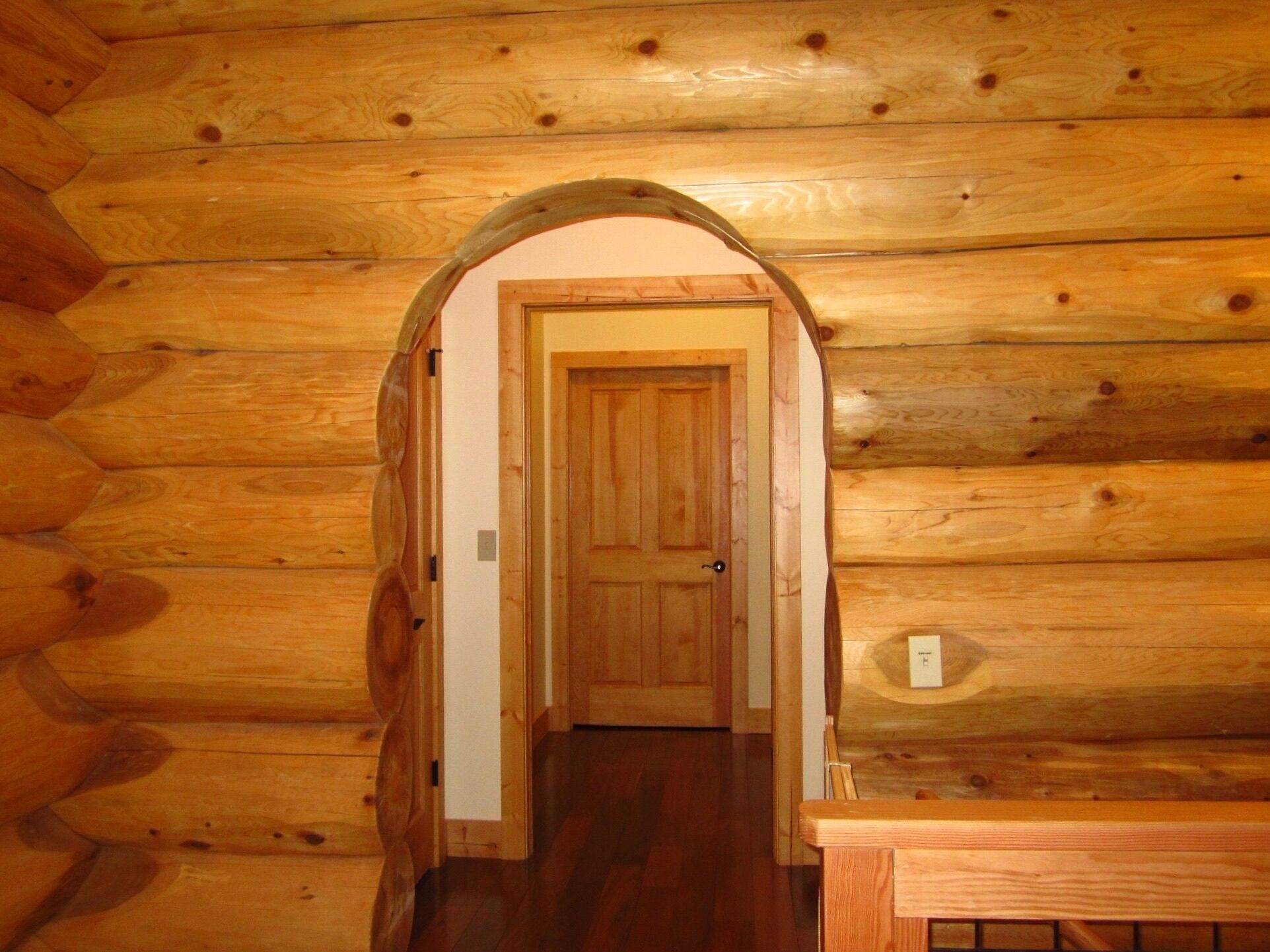 Ein rustikales Holzblockhaus im Inneren, mit einer zentralen Tür und einer hölzernen Bank.