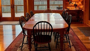 Ein Esszimmer mit Holzboden, einem großen Tisch und Stühlen, einer Kronleuchter und großen Fenstern.
