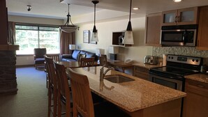 Una cocina moderna con encimeras de granito, electrodomésticos de acero inoxidable y un comedor con sillas y mesa de madera.