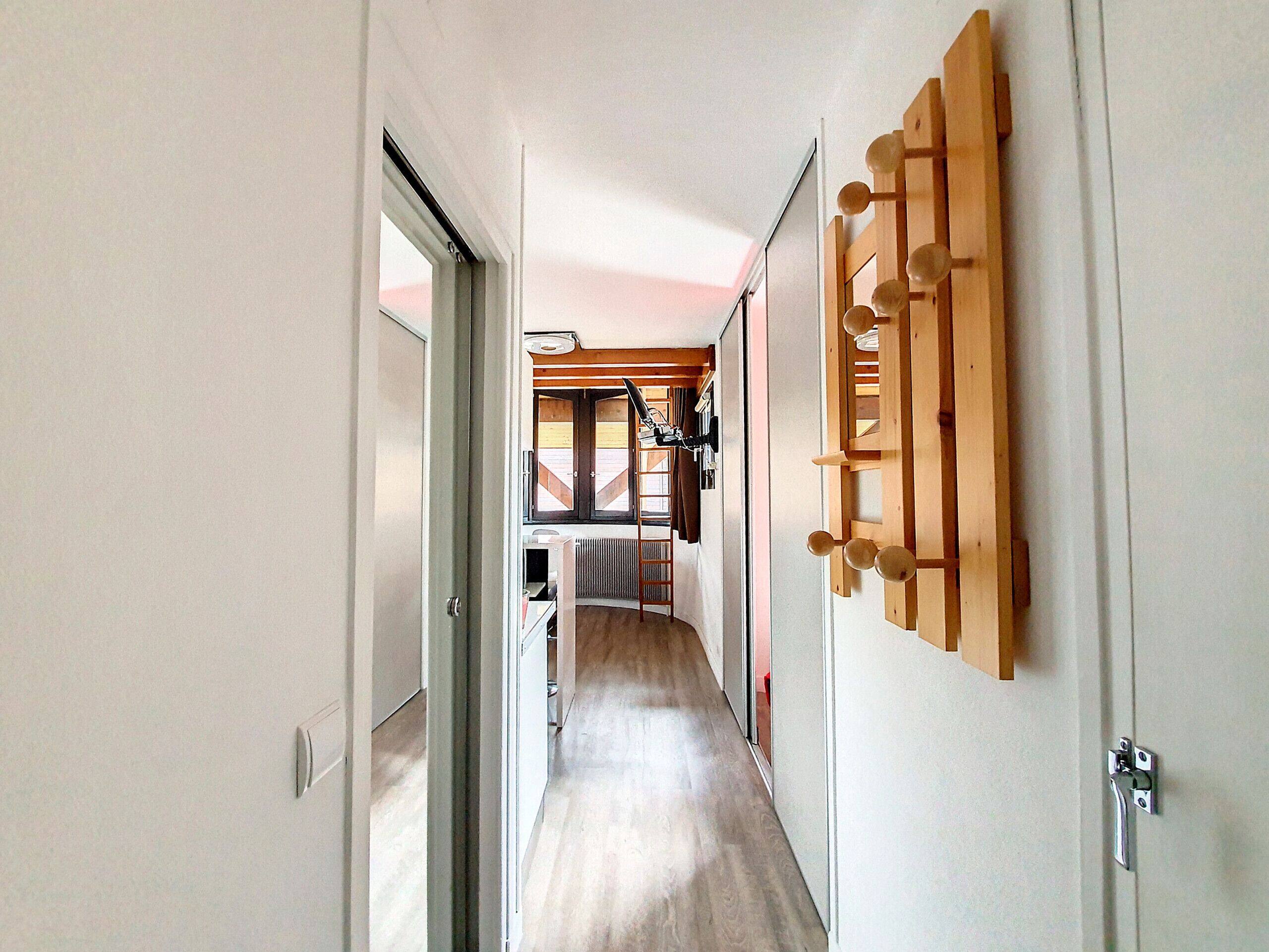 A hallway with a wooden coat rack, a radiator, and a view into a room with a window and a door.