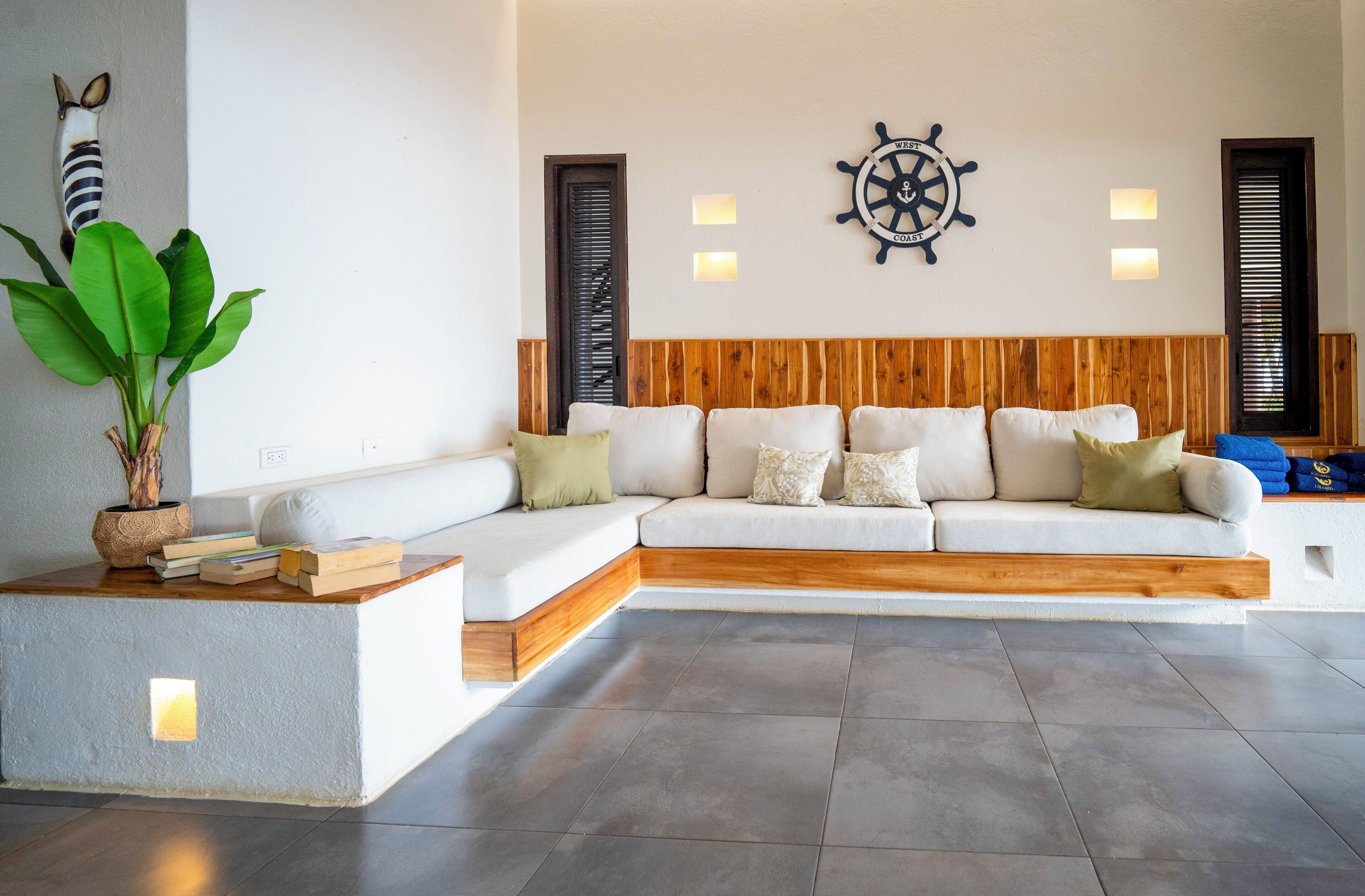 A modern living room with a white sectional sofa, wooden headboard, and a ship's wheel wall decoration.
