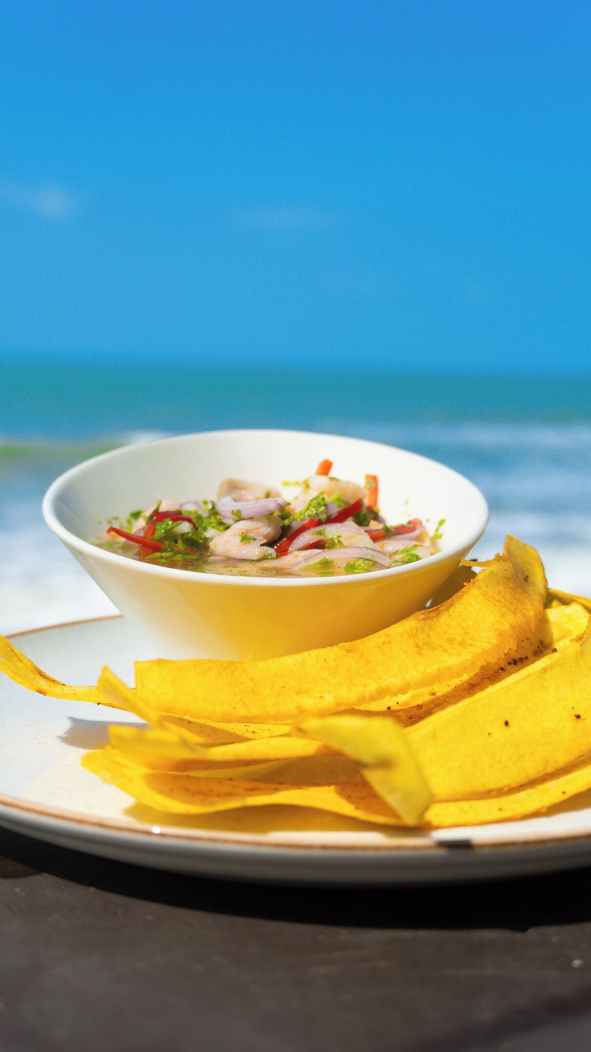 A bowl of seafood salad on a plate with yellow napkins, set against a beach background.