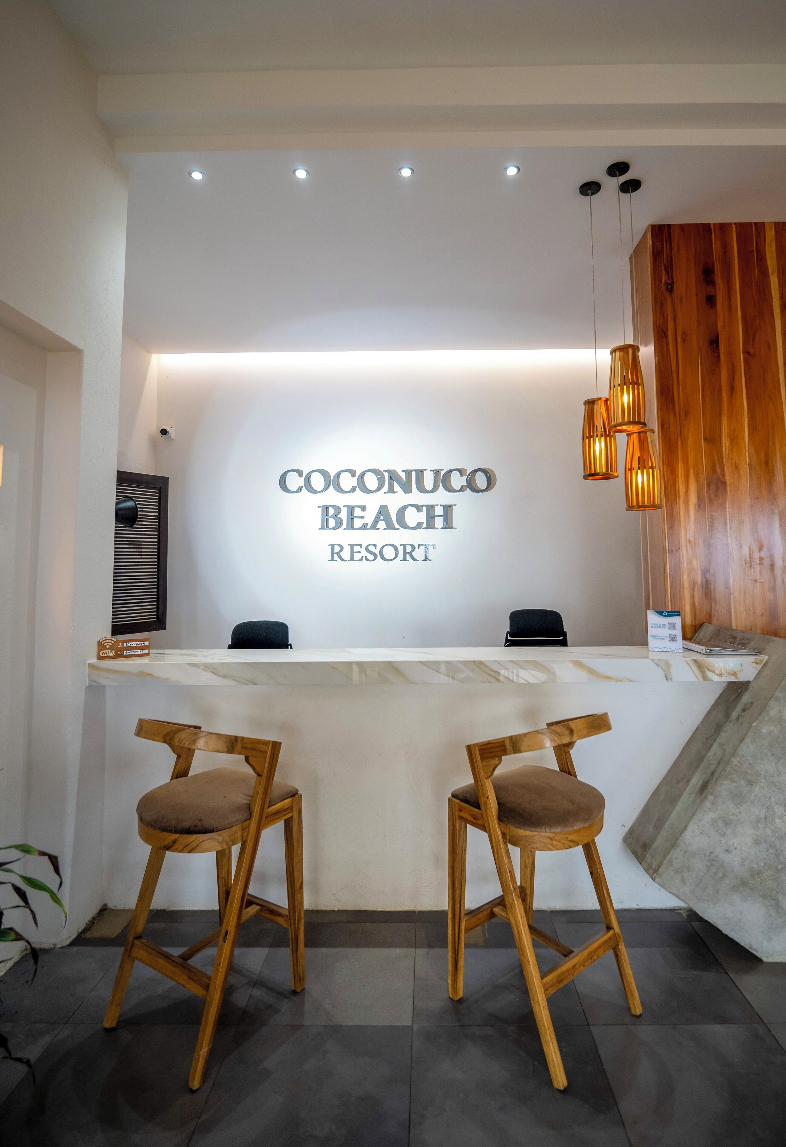 A reception desk at Coconuco Beach Resort with a marble top, two wooden bar stools, and a wooden wall panel.