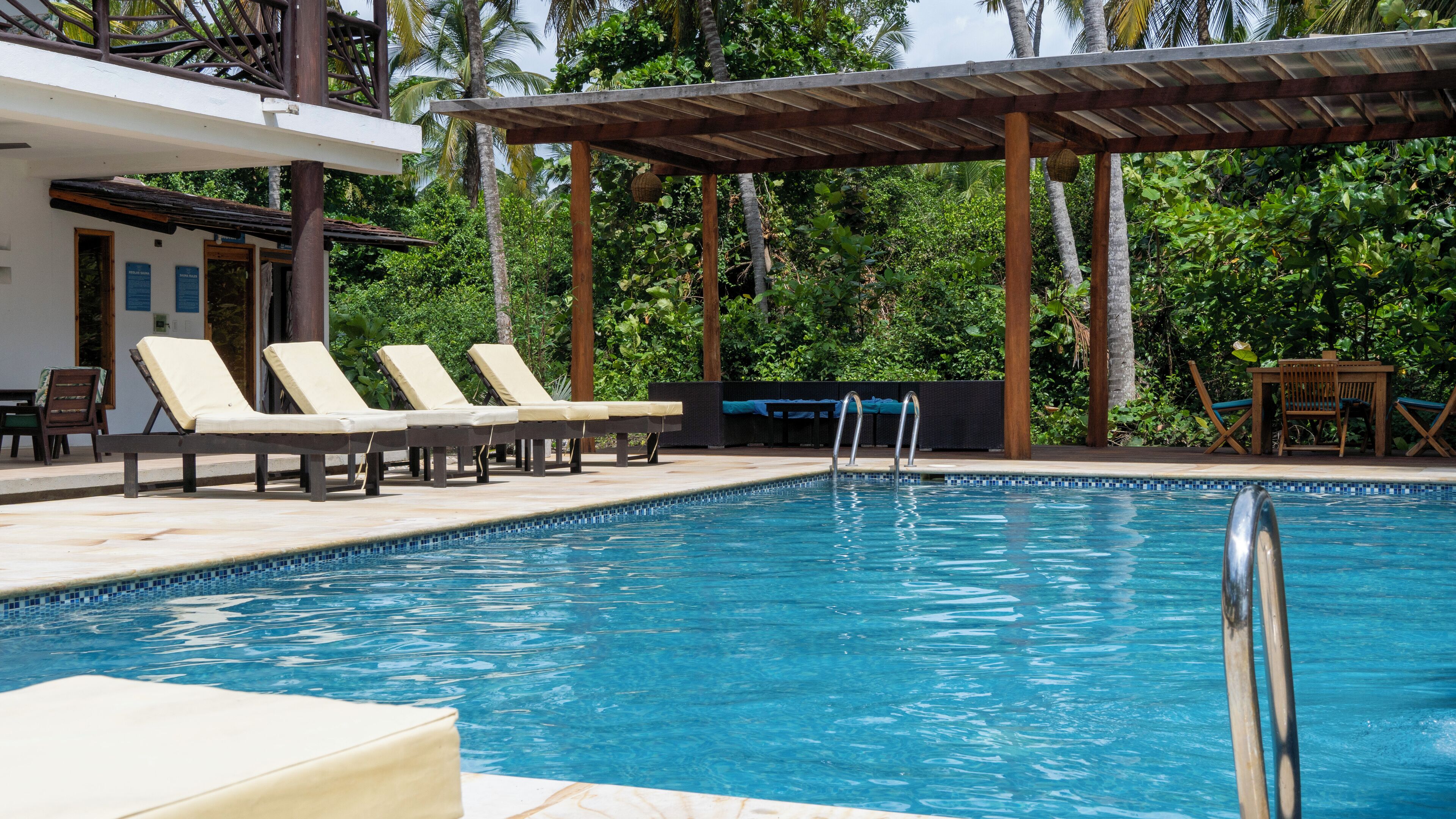A swimming pool with lounge chairs and a covered seating area, surrounded by lush greenery.