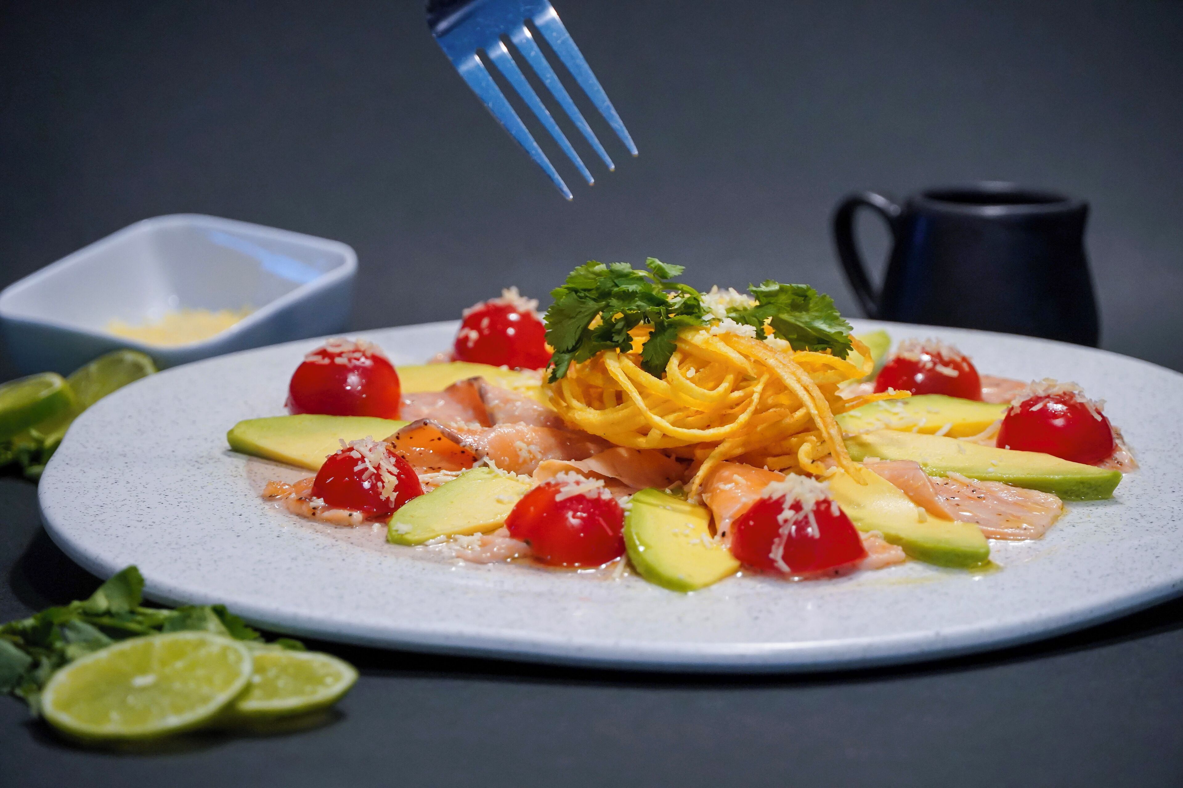A plate of pasta with cherry tomatoes, avocado, and cheese.