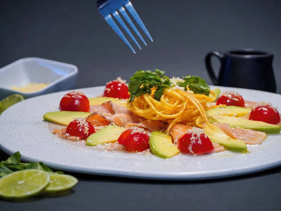 A plate of pasta with cherry tomatoes, avocado, and cheese.