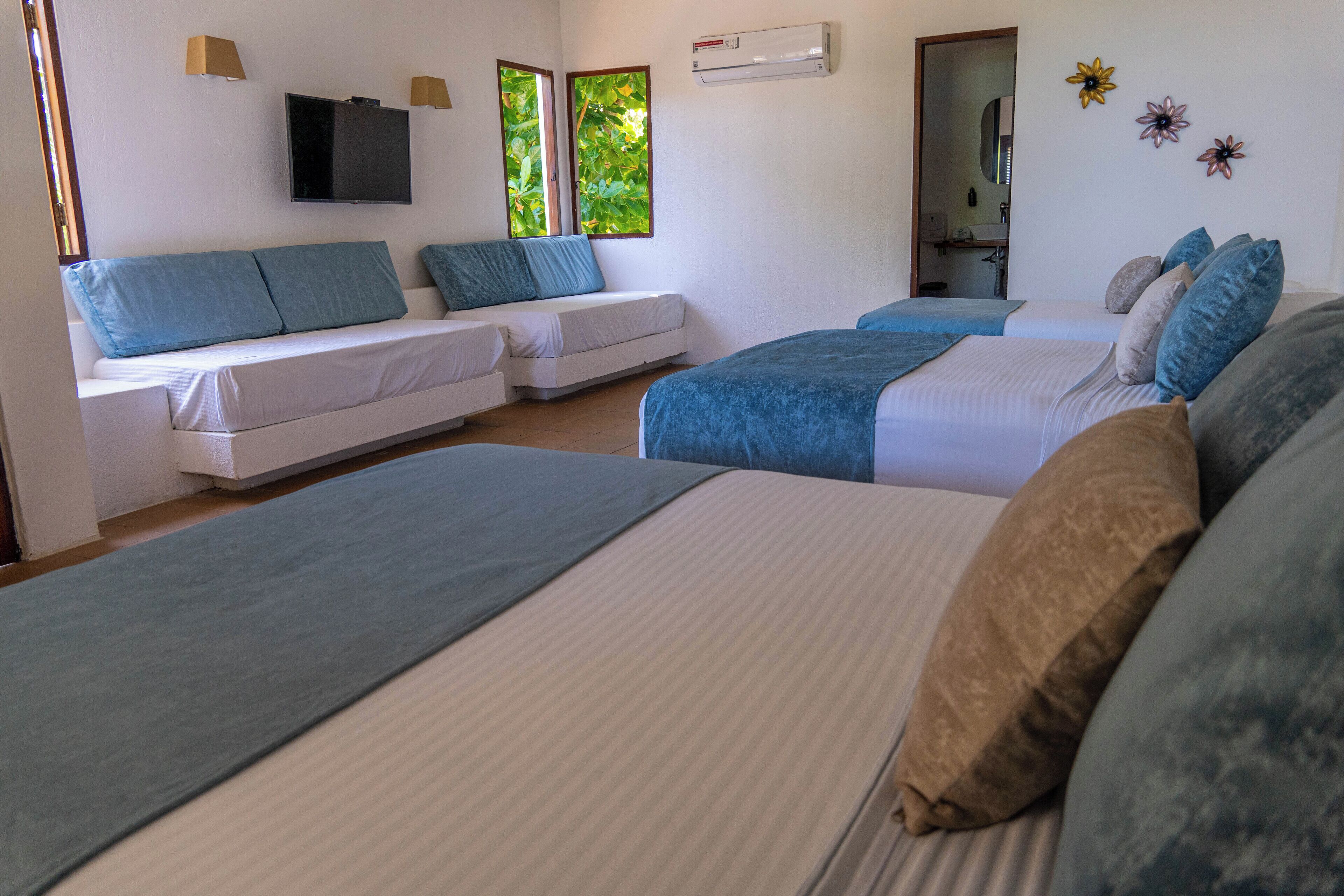 Habitación de hotel con dos camas, un sofá, una televisión y un ventanal con vistas a zonas verdes.