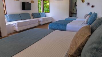 Habitación de hotel con dos camas, un sofá, una televisión y un ventanal con vistas a zonas verdes.