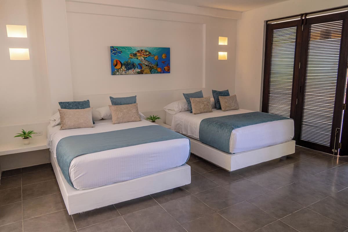 Un dormitorio con dos camas, un cuadro de una escena submarina y una puerta corredera.