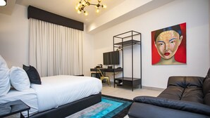 Ein modernes Hotelzimmer mit einem großen Bett, einem Schreibtisch mit Stuhl, einer Couch und einem Bild an der Wand.