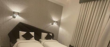 Habitación de hotel con dos camas, alfombra roja, escritorio y candelabro.