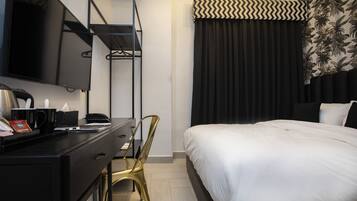 A hotel room with a bed, a desk with a chair, a television, and a wardrobe.
