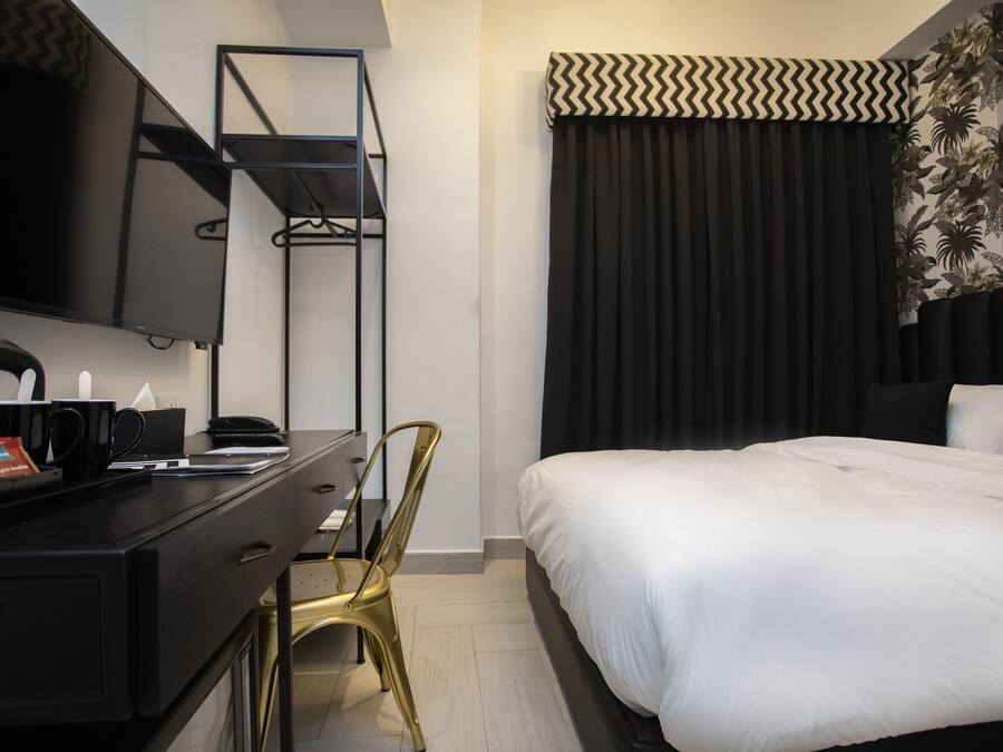A hotel room with a bed, a desk with a chair, a television, and a wardrobe.