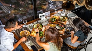 Eine Gruppe von Menschen speist in einem Restaurant, auf dem Tisch befinden sich verschiedene Gerichte, darunter Steak, Pommes und Salate.