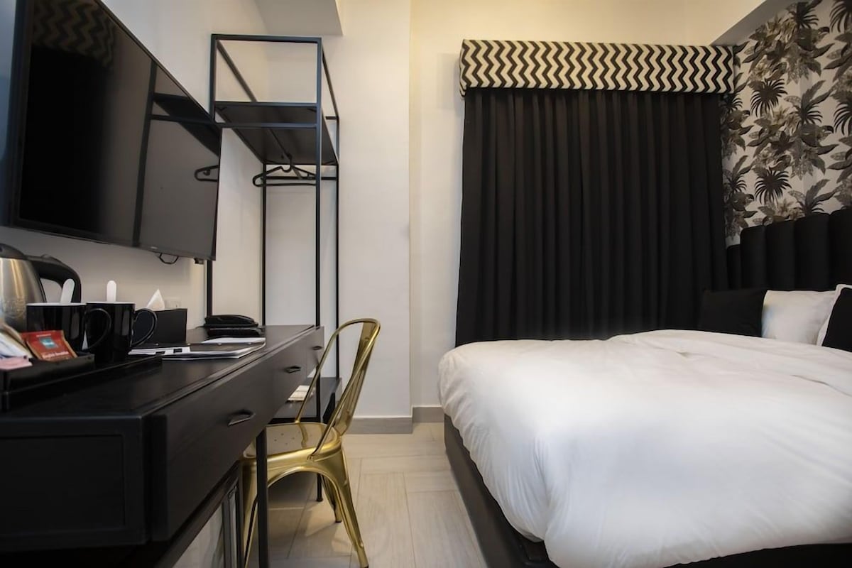 A hotel room with a bed, a desk with a chair, a television, and a window with curtains.