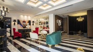Eine Lobby mit Schachbrettfußboden, roten und weißen Stühlen, einem türkisblauen Sessel, einer Chandelüster und einer Spiegelwand.