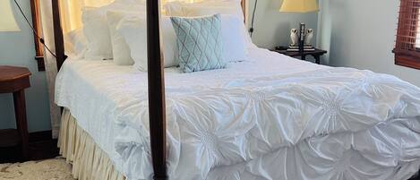 A four-poster bed with white bedding, a patterned carpet, and a framed picture on the wall.