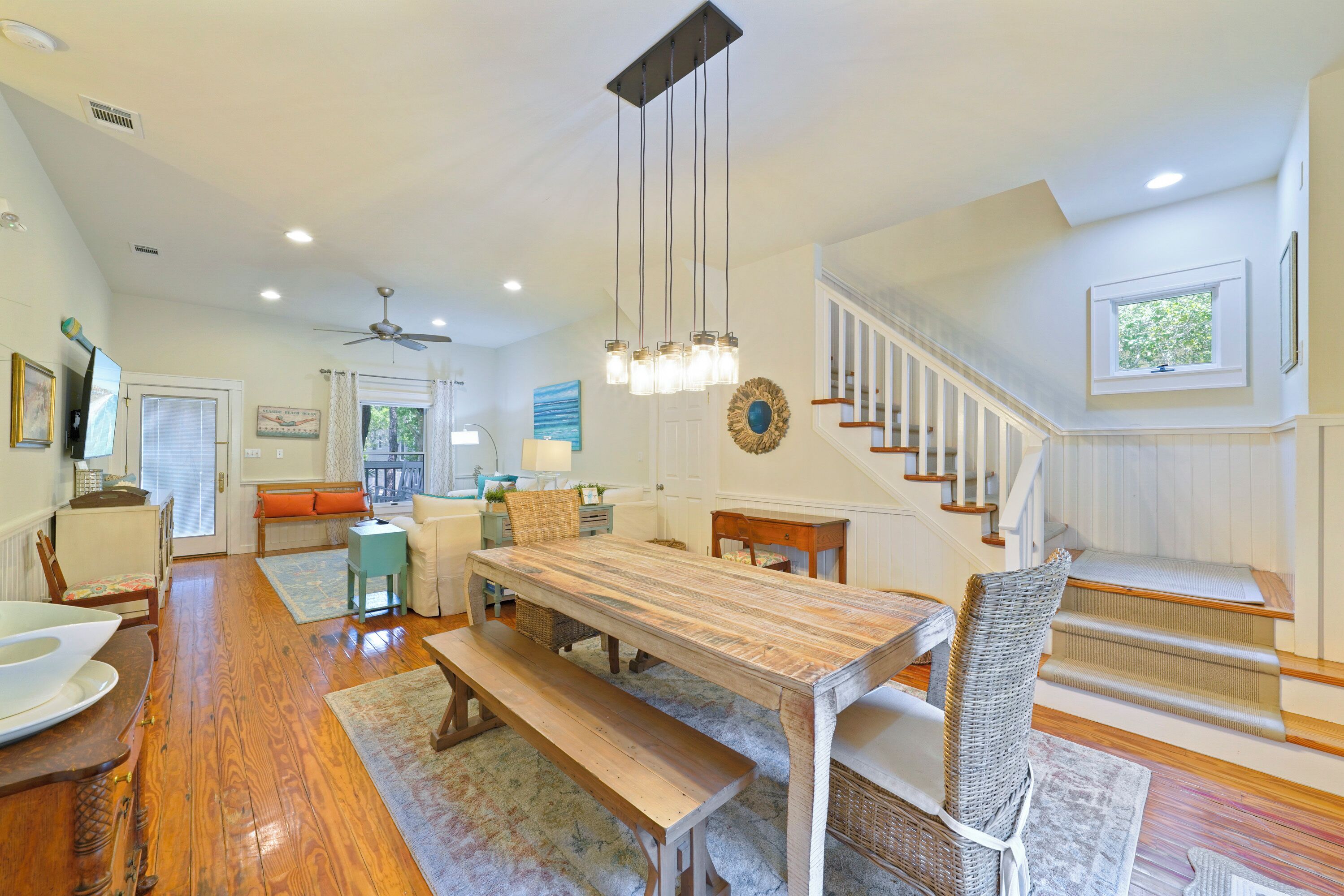 A spacious dining area with a wooden table and benches, a staircase with wooden steps, and a ceiling fan.