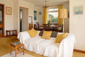 A living room with a white sofa, a small wooden table, and a dining area with a table and chairs.
