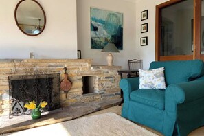 A living room with a stone fireplace, a teal armchair, and a painting on the wall.