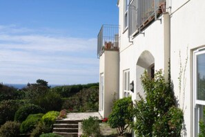 A two-story building with a balcony, a staircase leading to the entrance, and a view of the sea in the background.