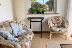 A cozy room with a wicker sofa and chair, a small table, and a window with plants.