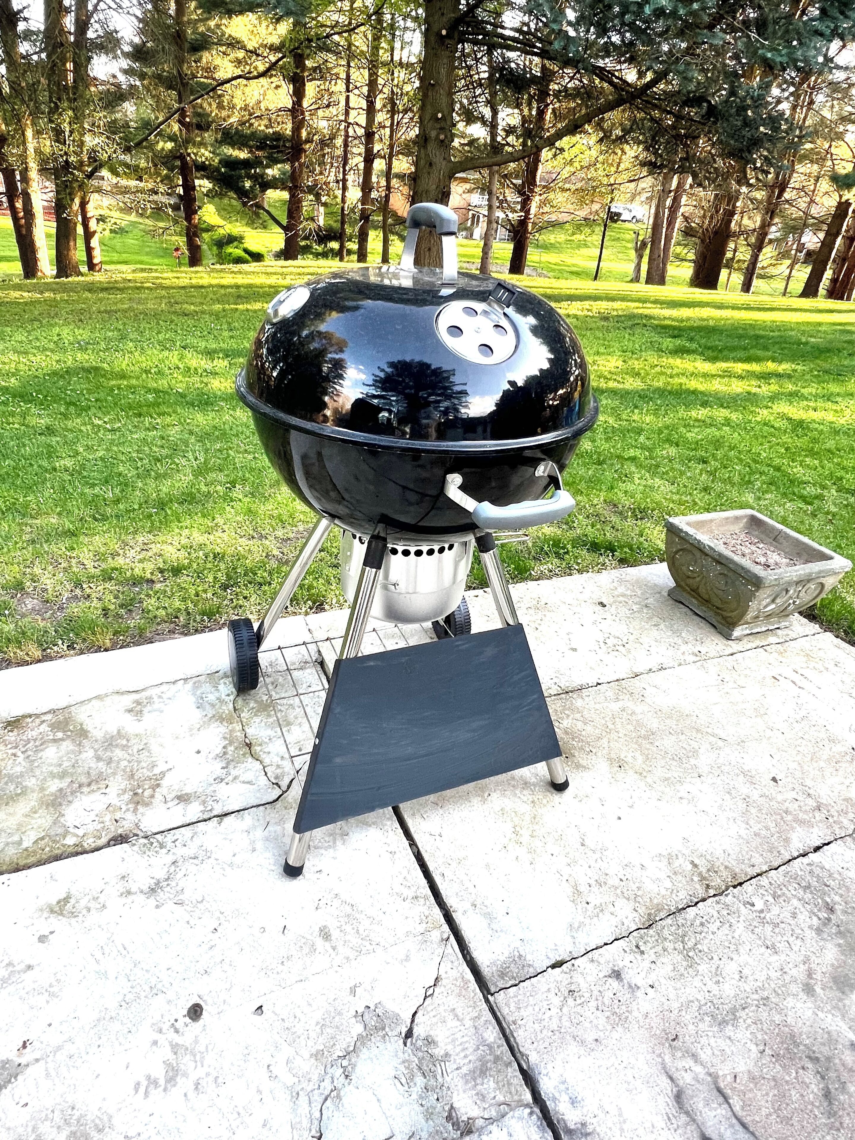 Un barbecue noir avec un support en métal et un plateau en pierre, installé sur une terrasse en béton.