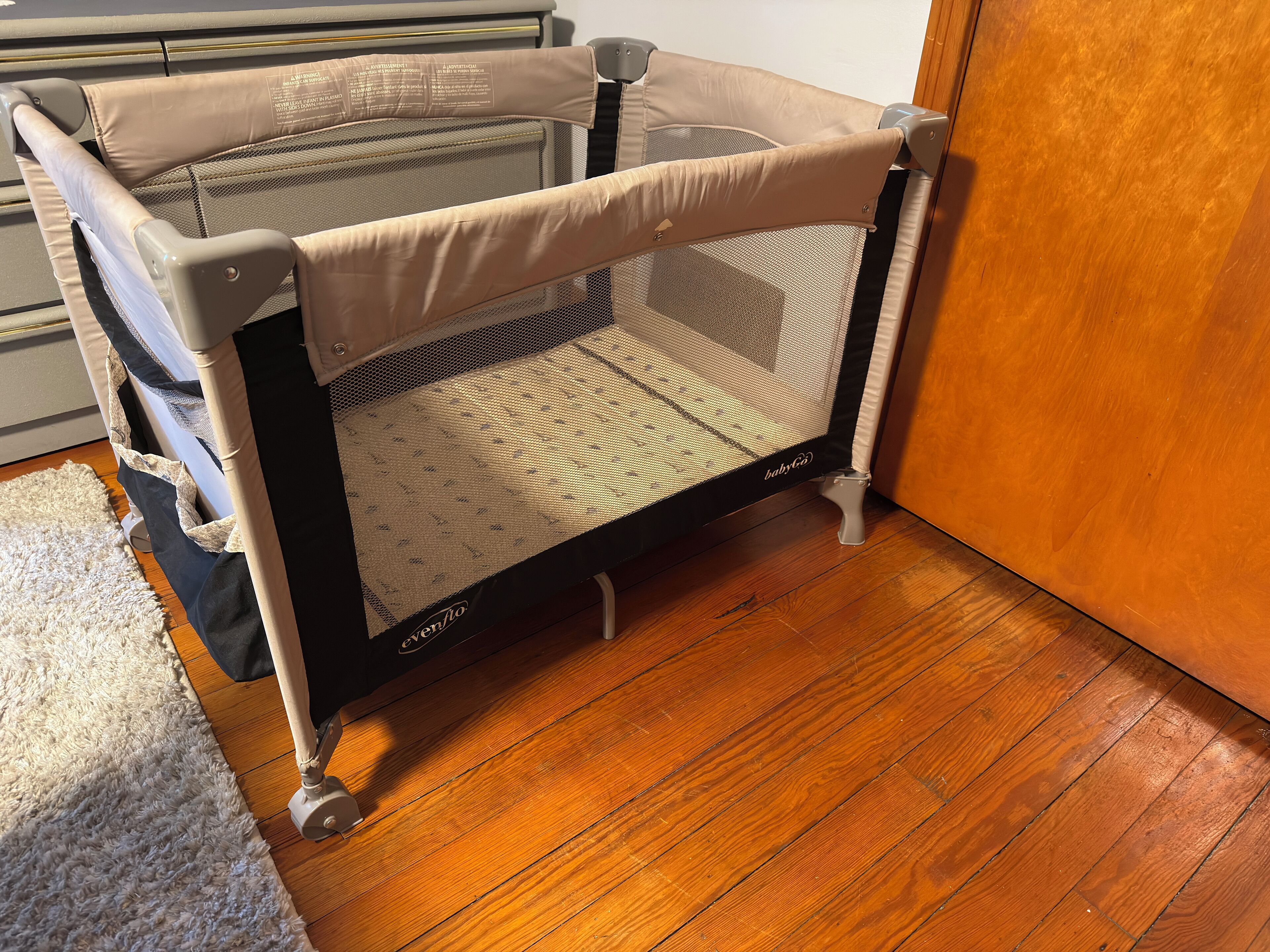 A baby gate with a mesh floor, attached to a wall, and a wooden floor in the room.