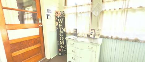A room with a wooden door, a welcome sign, a white dresser, and a patterned rug.