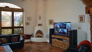 A living room with a fireplace, a television, and a large window. - Centrally Located 3 BR/3 Bath Adobe Home in Taos Mesa NM (El Prado)