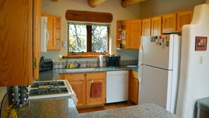 A kitchen with wooden cabinets, a stove, a refrigerator, and a window providing natural light. - Centrally Located 3 BR/3 Bath Adobe Home in Taos Mesa NM (El Prado)