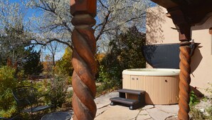 A hot tub with a wooden exterior, a stone patio, and outdoor seating. - Centrally Located 3 BR/3 Bath Adobe Home in Taos Mesa NM (El Prado)
