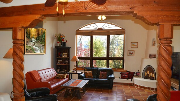 A living room with a fireplace, a large window, and a wooden ceiling. - Centrally Located 3 BR/3 Bath Adobe Home in Taos Mesa NM (El Prado)