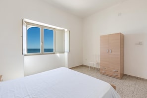 A bedroom with a bed, a wardrobe, a chair, and a window with a view of the sea.
