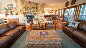 A cozy living room with leather sofas, a central woven ottoman, and a stone fireplace. - Canal Front, small dog ok, dock, screened private pool! (St. George Island)