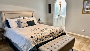Un dormitorio con una cama grande, un banco, una mesita de noche, un espejo y un armario.