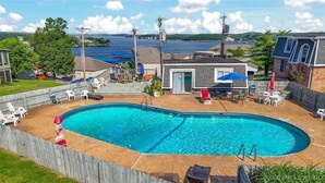 Un patio trasero con una piscina rectangular, rodeado por una valla de madera, y una zona de terraza con mobiliario exterior.