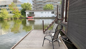 A wooden dock with two chairs, a small boat, and a building with a balcony in the background. - Central, cosy and modern appartment in Houseboat. Amsterdam Pur Sang. (Amsterdam)