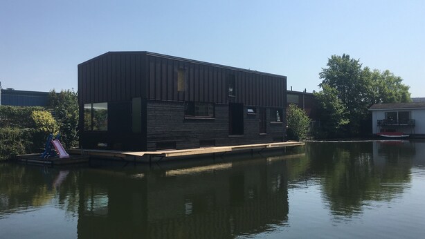 A modern houseboat with a flat roof, large windows, and a dock extending into a calm body of water. - Central, cosy and modern appartment in Houseboat. Amsterdam Pur Sang. (Amsterdam)