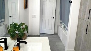 Een moderne badkamer met een wit wastafelmeubel, een spiegel, een potplant en een douche.