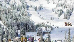 Een besneeuwde skioord met een skilift, chalets en een berg op de achtergrond.