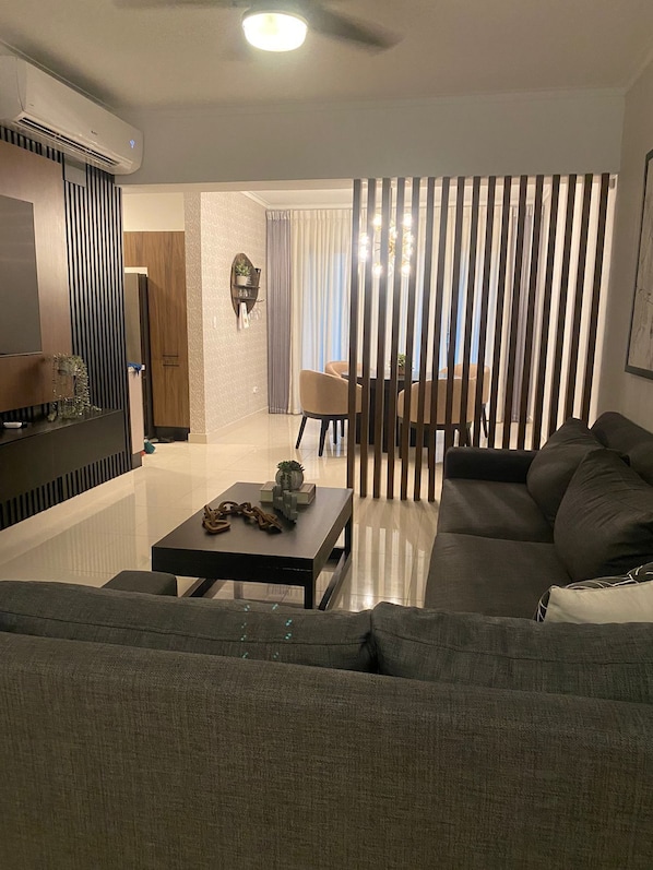 A modern living room with a sofa, a coffee table, and a dining area with a table and chairs.