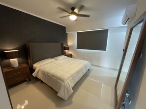 Un dormitorio con cama, mesitas de noche, ventilador de techo, aire acondicionado y ventana.