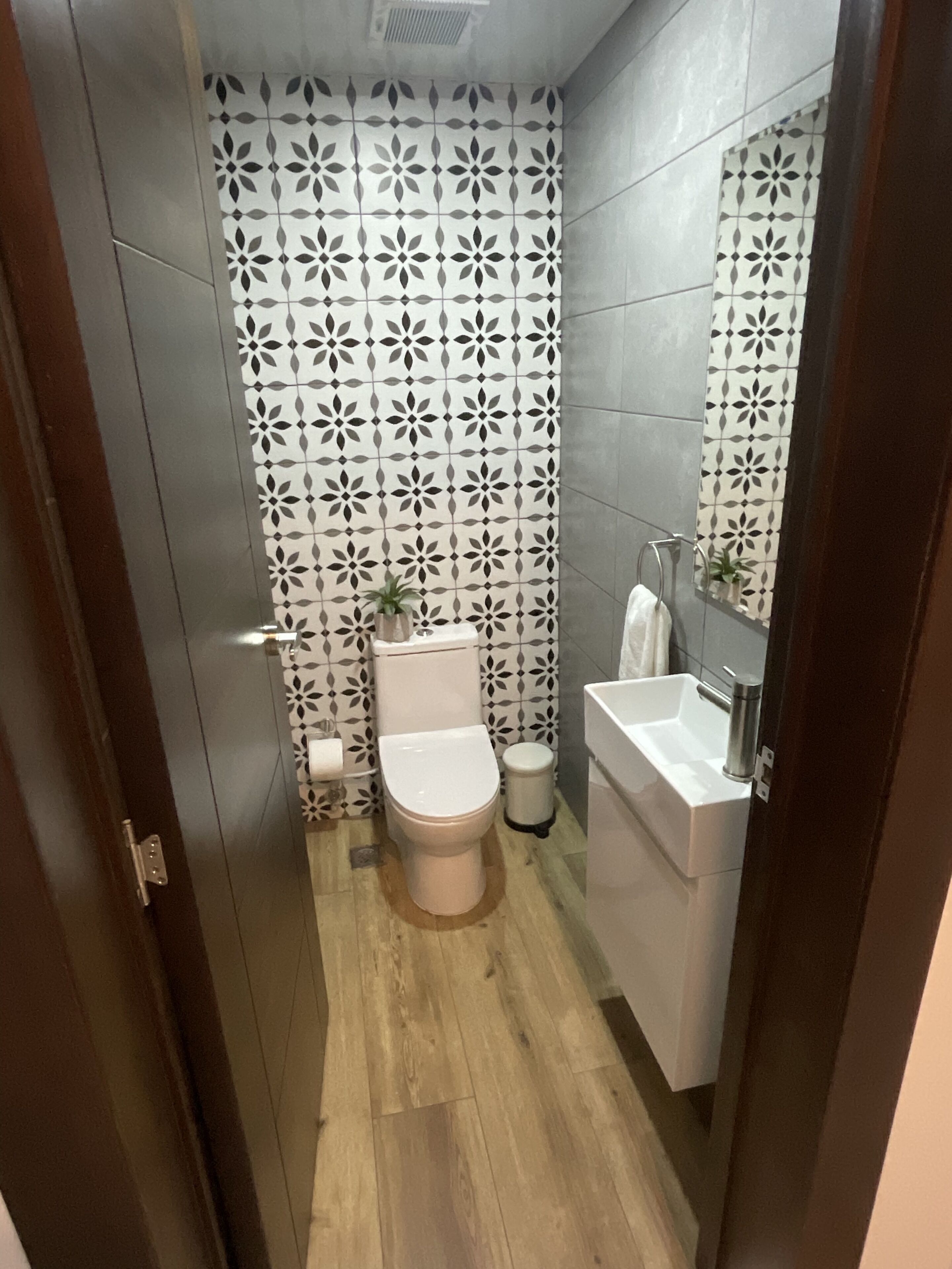 Une petite salle de bain comprenant des toilettes, un lavabo et un miroir. Les murs sont recouverts de carreaux disposés selon un motif géométrique.