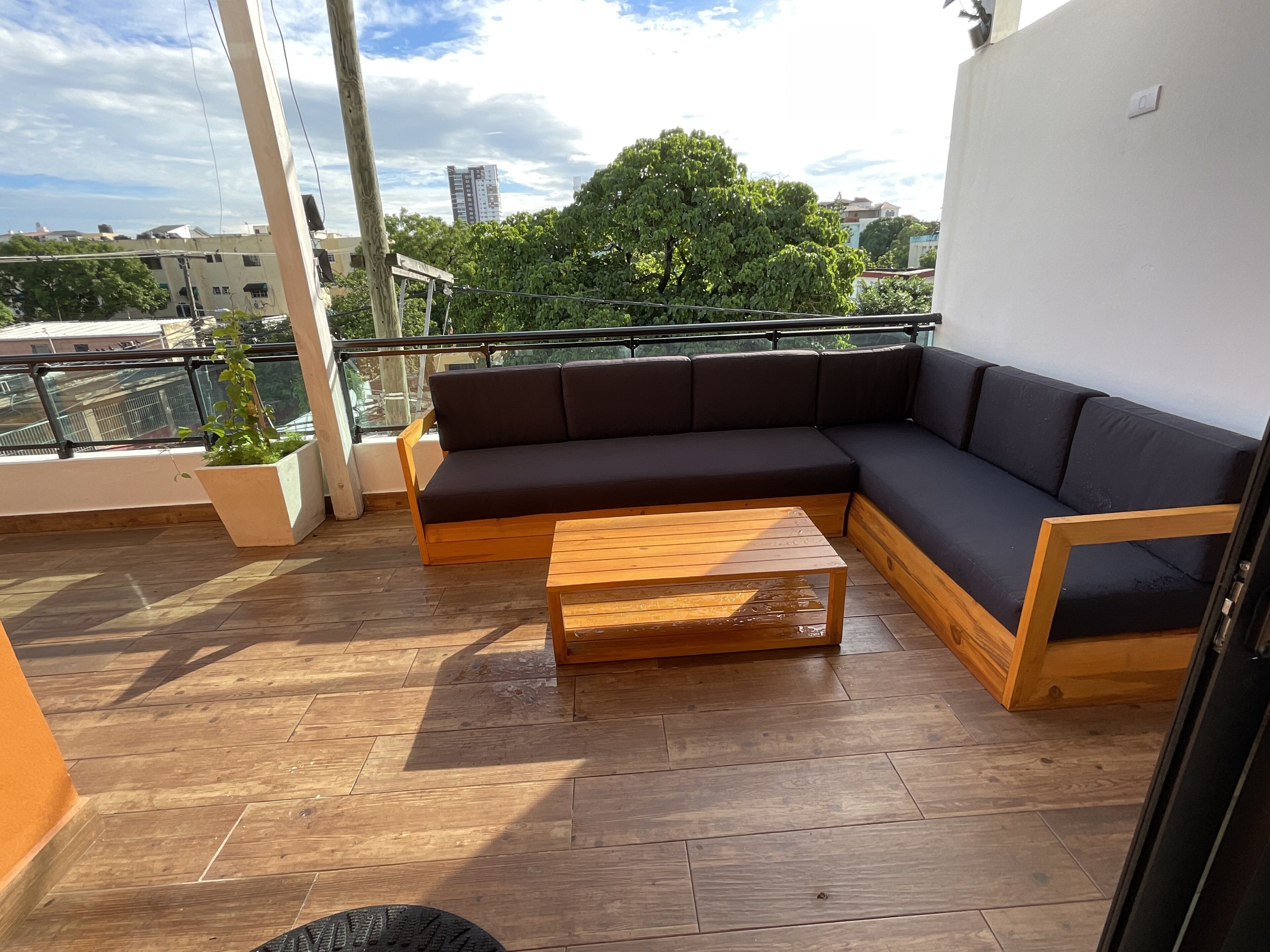 Un balcón con piso de madera, un sofá oscuro y una mesa de centro de madera.