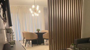 A modern living room with a dark coffee table, a sofa, and a dining area with a table and chairs. - Brand New luxury condo in Alma Rosa 1, large terrace (Santo Domingo Este)