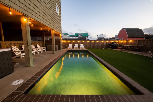 A swimming pool with a wooden deck and lounge chairs, surrounded by a wooden fence and a grassy lawn.
